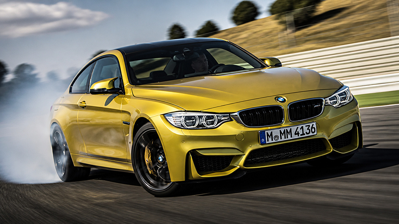 Gelber BMW M4 driftet auf Rennstrecke, Rauch steigt von den Reifen auf, Fahrer im Fahrzeug sichtbar.