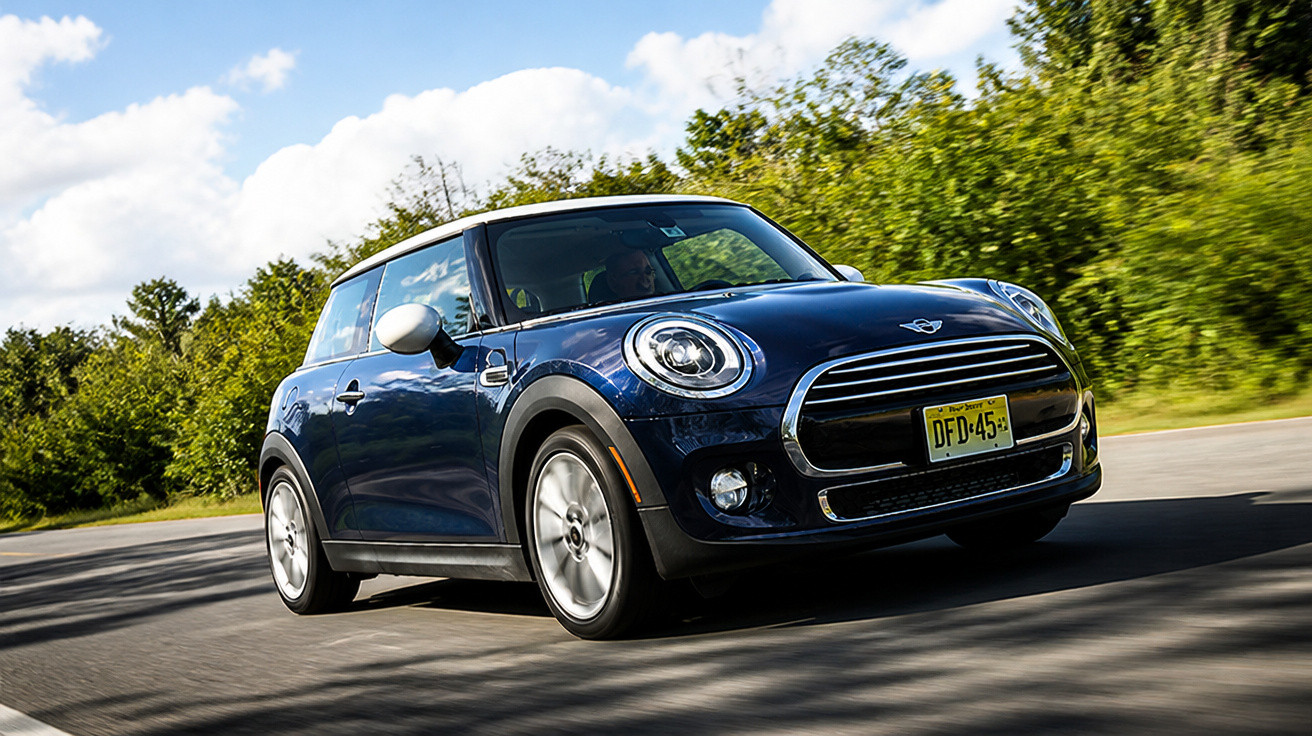 Blauer Mini Cooper fährt auf Straße mit Bäumen und blauem Himmel im Hintergrund, sonniger Tag.