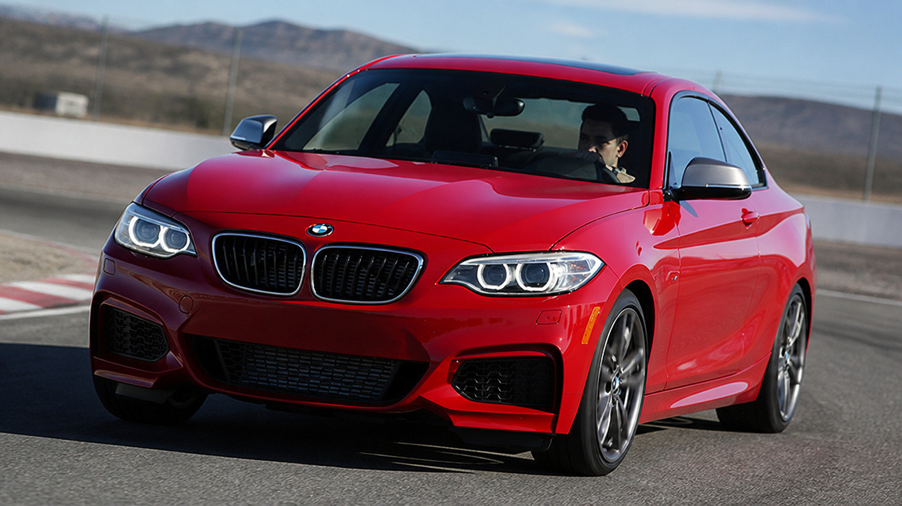 Rotes BMW Coupé fährt schnell auf einer Rennstrecke bei klarem Himmel.