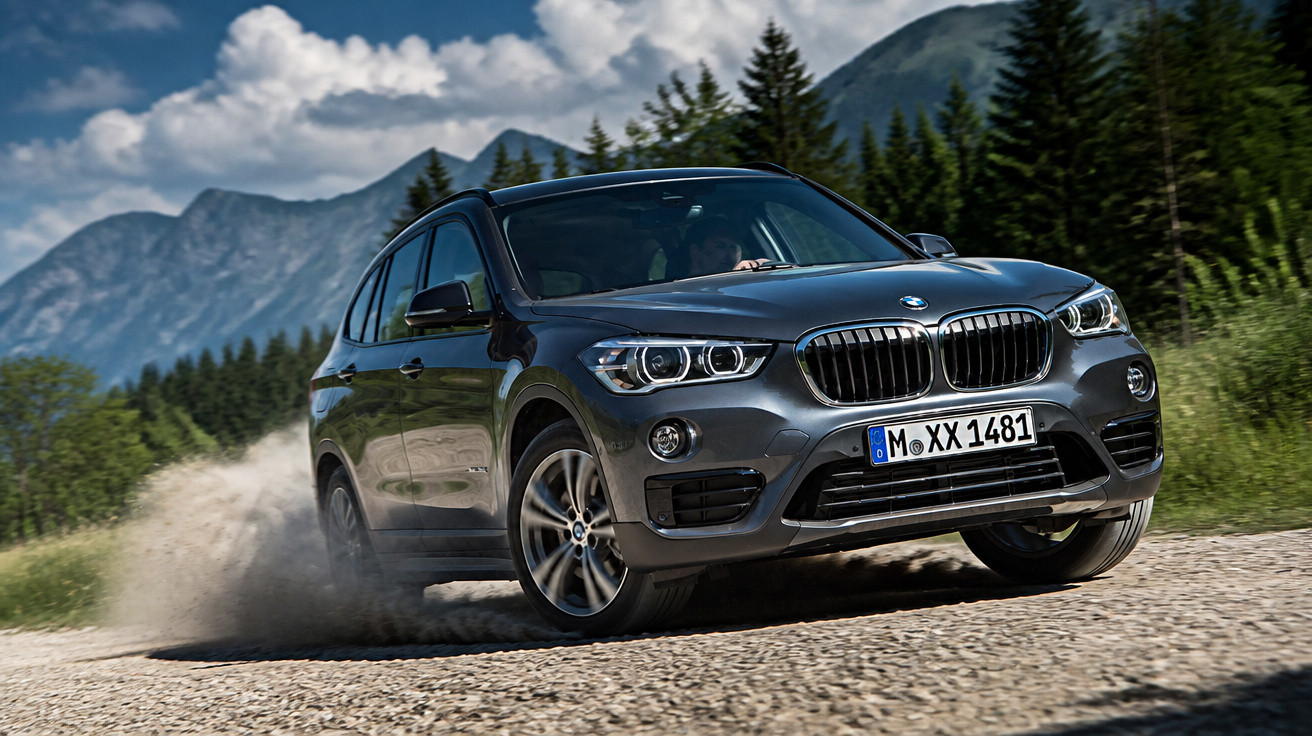 Schwarzer BMW SUV fährt auf einer Schotterstraße mit Bergen und Nadelbäumen im Hintergrund.